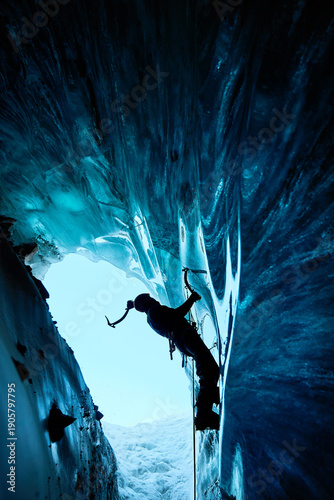 Man climbing frozen ice cave in winter mountains