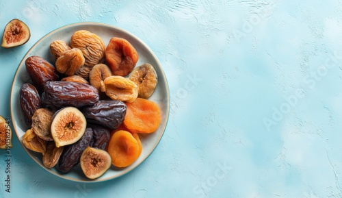 A plate of dried fruits, including dates, figs, and apricots, on a light blue textured background.