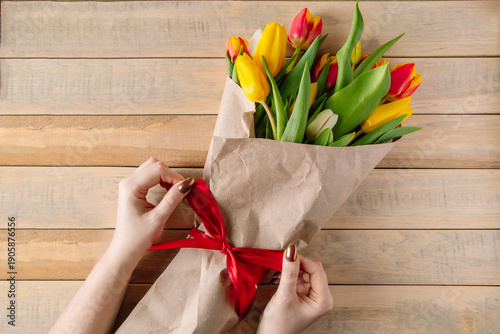 Obraz na płótnie Woman florist ties red bow on large bouquet of colorful tulips