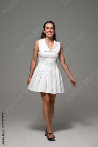 Happy brunette young woman with make-up, dressed in a white dress, posing in studio, over white bright background. 