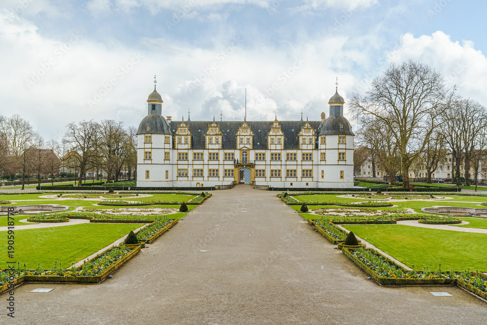 Obraz premium A large white building of Neuhaus Castle in Paderborn Germany with a courtyard in front of it. The courtyard is surrounded by a gravel path and has a lot of flowers