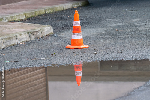 Fotografia an orange traffic cone with white reflective stripes standing on asphalt, perfectly mirrored in a puddle of water in the foreground