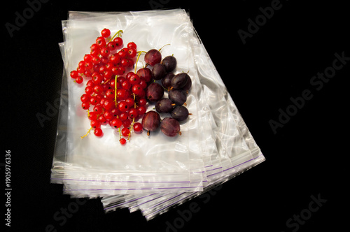 Currants and gooseberries in airtight ziplock bags on dark background, top view