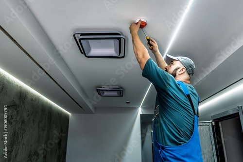 Professional master in blue overalls is installing or repairing fire alarm maintenance