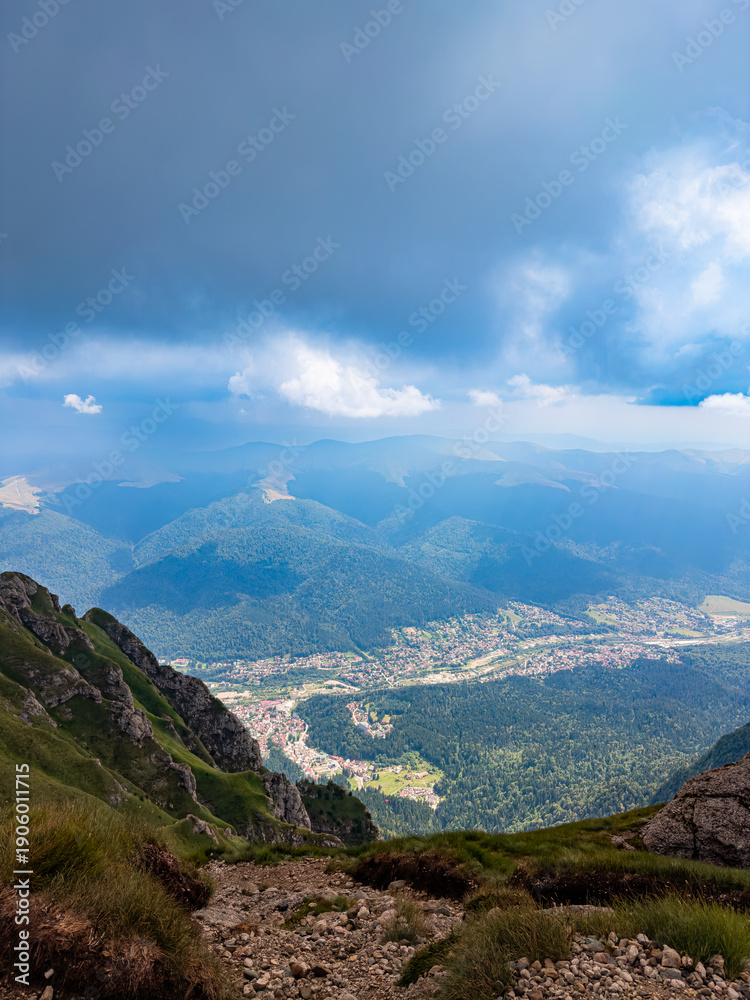 Fototapeta premium Mountain valley view toward Busteni Romania. Wide mountain valley view descending toward Busteni town beneath heavy clouds in Bucegi Mountains.