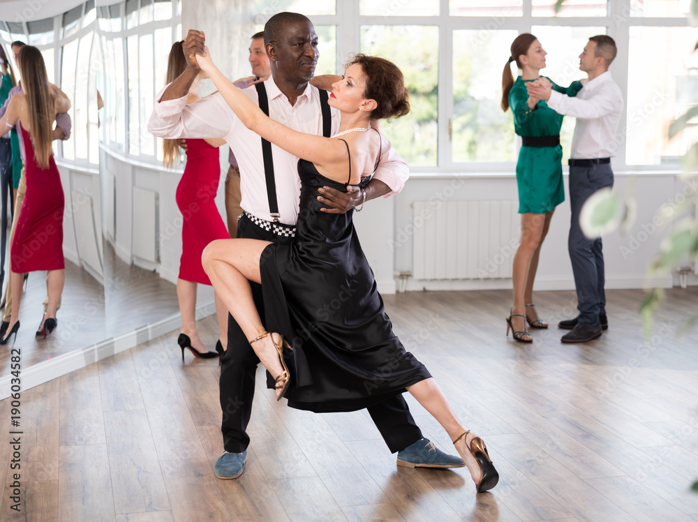 Fototapeta premium Dynamic middle-aged male and female attendees of dancing courses doing waltz in group