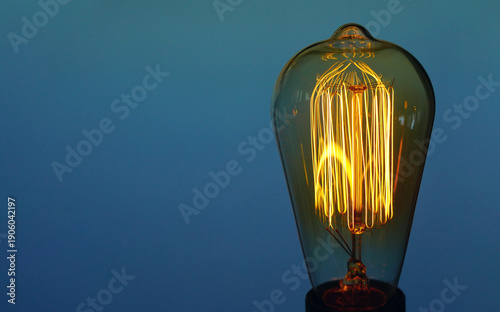 An old vintage lamp with an incandescent filament against a blue sky shines with a warm and soft yellow light
