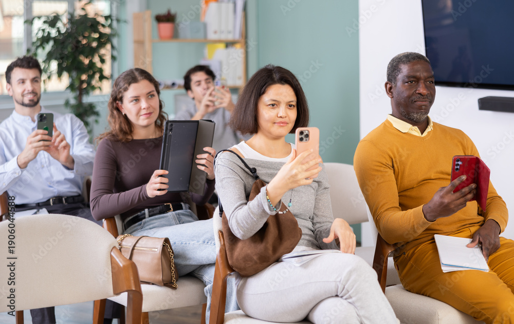 Fototapeta premium Young woman uses mobile phone to scan QR code or take photo during lecture in lecture hall