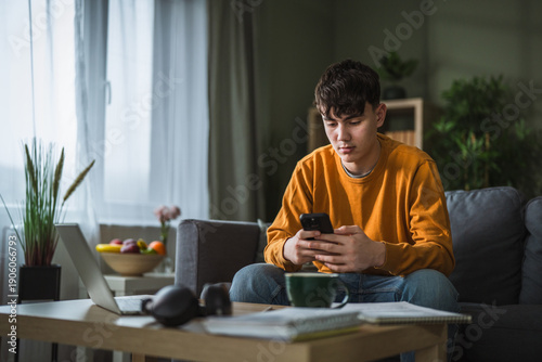 Quadro em tela Teenage boy using smart phone, distracted from studying at home
