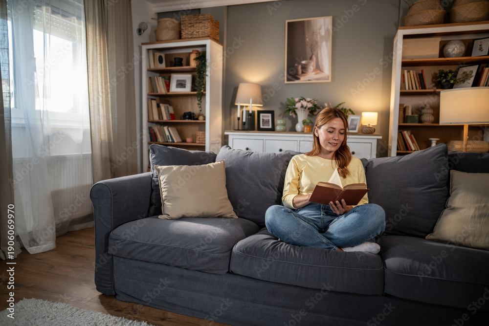 Obraz premium Young woman relaxing on sofa reading book at home