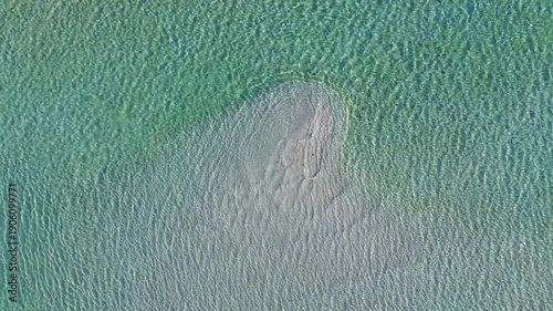 Aerial top-down view of turquoise water looping over a submerged sandbar