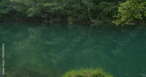 Crystal clear emerald water of the Una River flowing through dense green forest in Bosnia and Herzegovina. Scenic Balkan landscape with calm turquoise surface and tree reflections, pristine freshwater