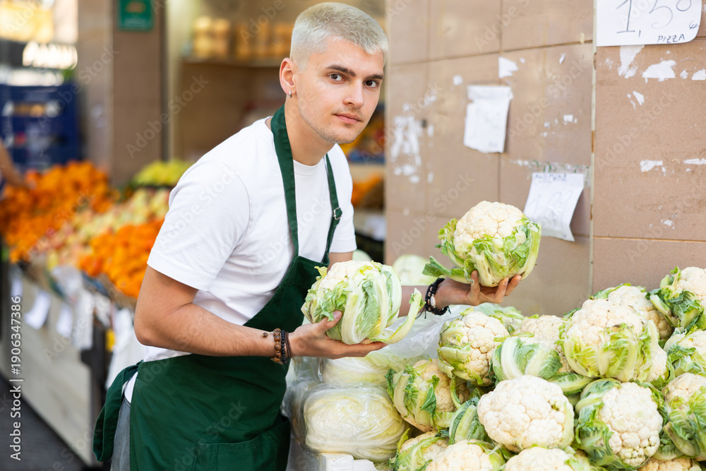 Fototapeta premium Grocery store employee places ripe broccoli on a display case at a street store