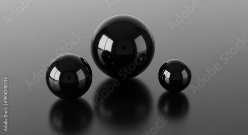 Three highly polished, dark spheres of varying sizes rest upon a reflective surface.