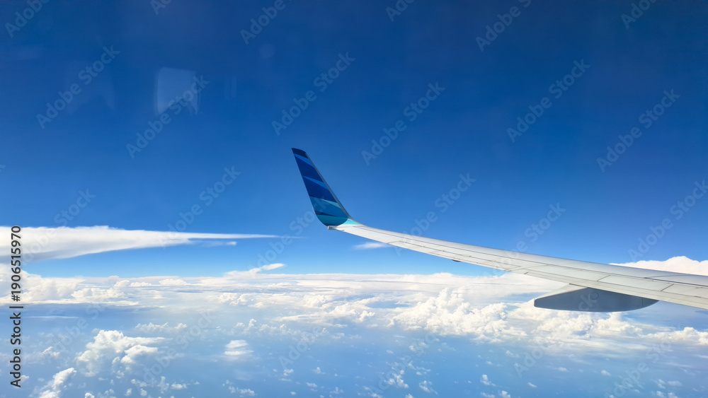 Fototapeta premium Airplane wing flying above clouds under a bright blue sky