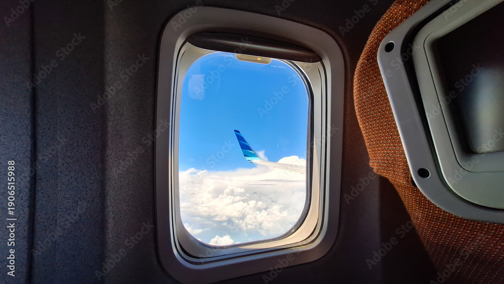 Fototapeta premium Airplane window view showing wingtip above clouds under a bright blue sky