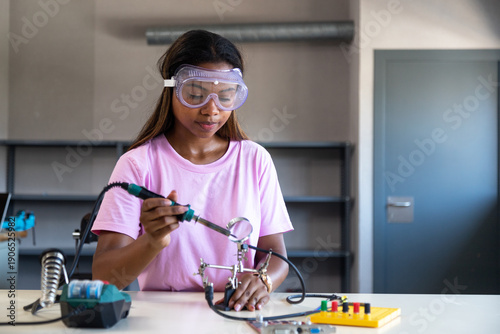 Obraz na plátne Young woman soldering electronics in a technology workshop