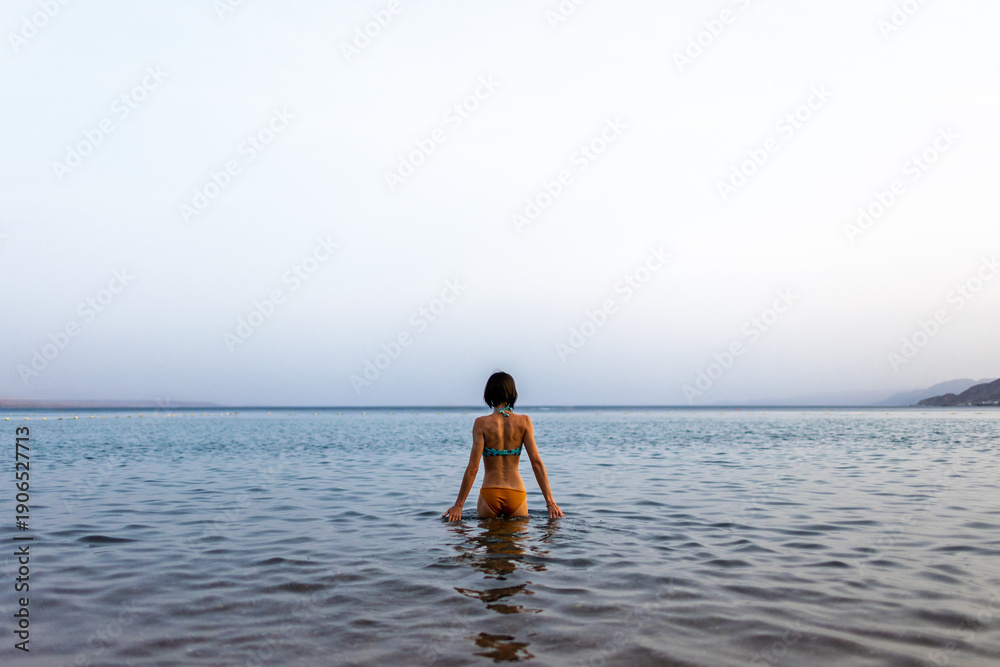 Obraz premium Slender girl in a swimsuit enjoys swimming in the sea. The girl relaxes and swims in the waters of the Red Sea in Israel.