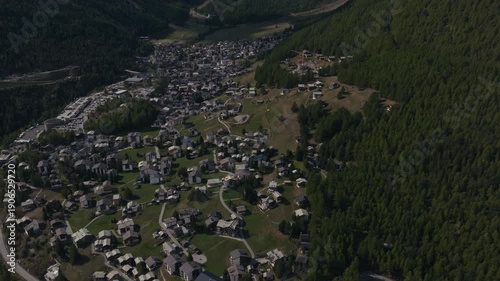 Aerial drone footage of the town of Saas-Fee with views over Allalin, Saas-Allmagell and Saas-Grund on a clear bluebird autumn day. Green valley floor contrasts with snow-covered alpine peaks.