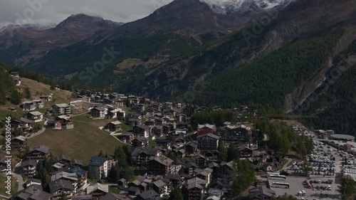 Aerial drone footage of the town of Saas-Fee with views over Allalin, Saas-Allmagell and Saas-Grund on a clear bluebird autumn day. Green valley floor contrasts with snow-covered alpine peaks.
