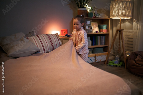 Bilde på lerret Caucasian child girl going to bed in cozy bedroom, taking blanket with focused e