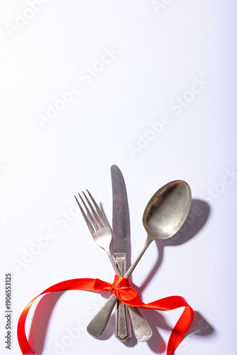 Overhead view of cutlery tied tightly with red ribbon below copy space over white background
