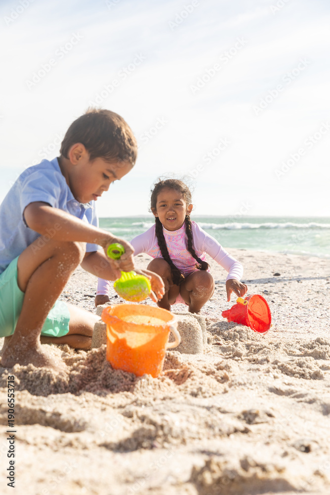 Fototapeta premium brother and sister collecting sand in buckets while playing at beach on sunny day
