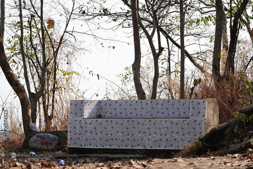 A concrete structure covered with patterned tiles is set amidst a wooded area with sparse trees and dry foliage.