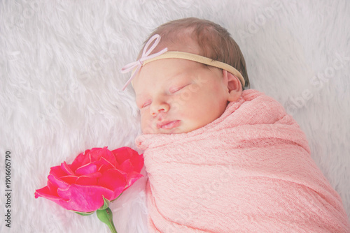 Photos Sleeping newborn baby girl in pink wrap with a rose flower on white fur backgrou