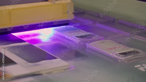 4K footage of a UV flatbed printer simultaneously printing an image on several silicone mobile phone case. Industrial digital printing process for custom smartphone accessory production.