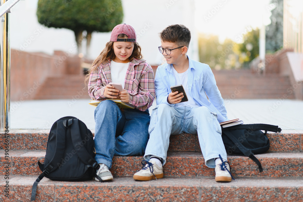 © Serhii - School children sitting on steps using smartphones