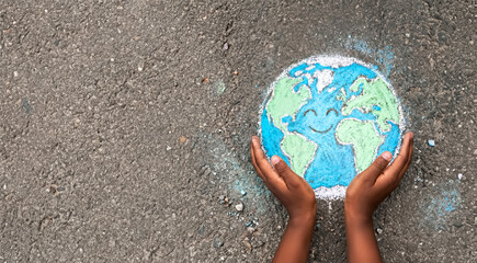 Above View of Child’s Hands Cupping a Cute Smiling Earth Drawing on Asphalt