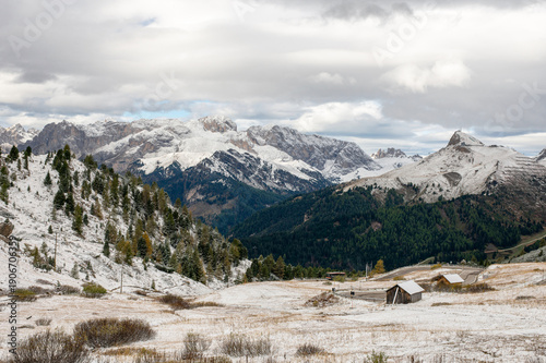 Billede på lærred Snow covered alpine valley with wooden cabins and winding road in the Dolomites