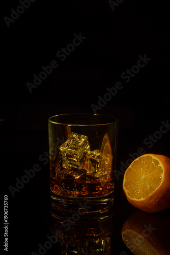 Drink in a glass with ice cubes and lemon on a dark background. Different light. Low key.