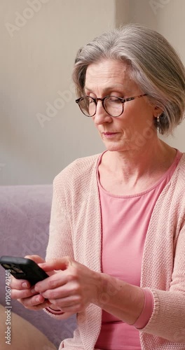 Mature old 60s woman, older middle aged female customer holding smartphone using mobile app, texting message, search ecommerce offers on cell phone technology device sitting on couch at home