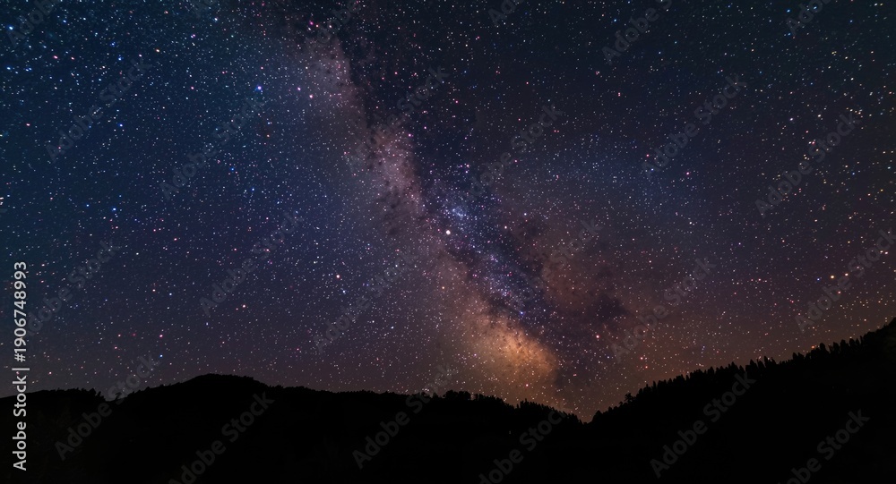 Fototapeta premium Celestial scene displaying vibrant constellations in a starry night with mountainous silhouettes and significant copy space