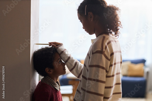 Billede på lærred Black girl teenager measuring height of Black boy child against wall using penci