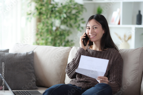 Happy asian woman talking on phone about letter looking at you