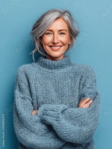 A cheerful elderly woman in a blue sweater is positioned against a solid blue backdrop.