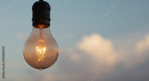 Glowing light bulb in front of a lightly blurred sky backdrop