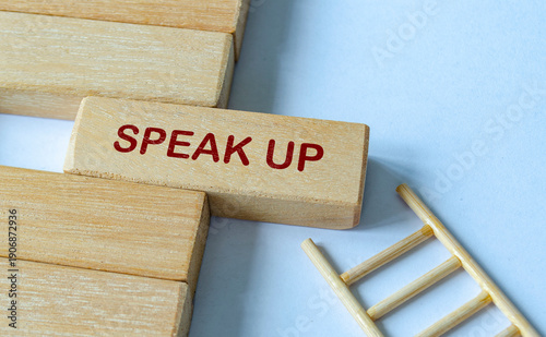SPEAK UP text on wooden blocks with ladder representing accessible reporting and open dialogue.