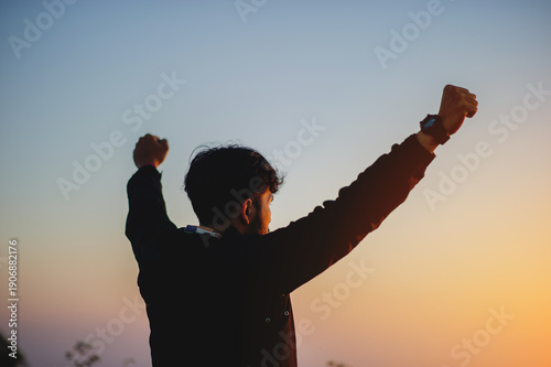 Fotografija The victory and freedom in life of the man who raises his arms and clench his fists above his head, having goals and achieving success