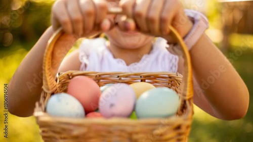 Close-up of little girl holding a wicker basket with pastel easter eggs in a sunny park, spring holiday celebration with bokeh background.