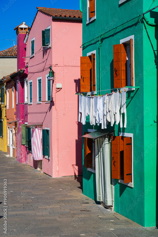 Fototapeta premium Colorful buildings with clothes drying on a sunny street in a vibrant neighborhood. Burano, Venetian Lagoon, Italy