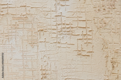 Close-up of a heavily weathered wall with peeling white paint revealing rough yellow-brown stucco, creating a textured, grunge-style background conveying age, decay, and urban wear