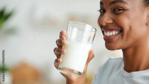 Smiling young black woman drinking a glass of milk at home, healthy dairy nutrition and wellness lifestyle with copy space.