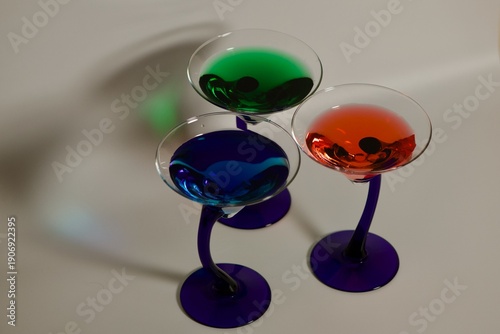 three blue stem Martini glasses with red, blue and green cocktails with shadows