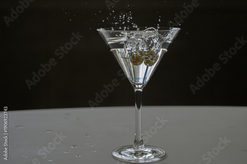 Martini cocktail splash with olive garnish falling into it action freeze, isolated on a black and white background, Portrait shot, two olives cocktail