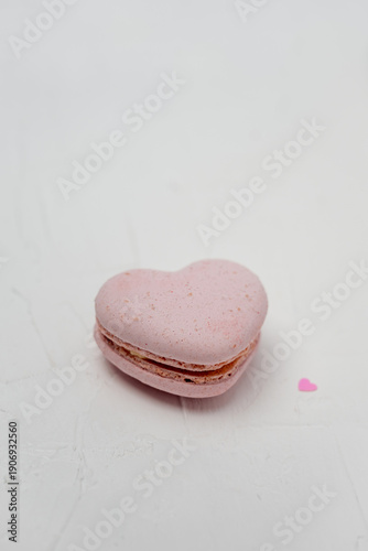 Pink heart-shaped macaron, symbolizing love and romantic sweetness, sitting on a textured white background with a small decorative heart, creating a charming and delightful dessert concept
