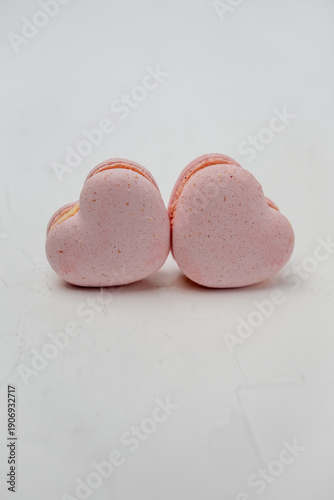 Two pink heart-shaped macarons on a white background, delicate meringue cookies with creamy filling evoking love, romance and sweet celebrations like Valentine's Day or anniversaries
